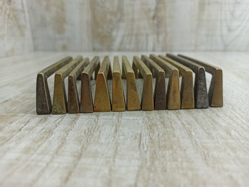 Op de afbeelding: Een set van 18 messing ladegrepen met een driehoekige vorm. De grepen zijn in een rij gerangschikt en hebben een licht verweerde afwerking.