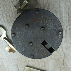 May include: A black metal lock with a keyhole and several rivets. The lock is on a light wood surface.