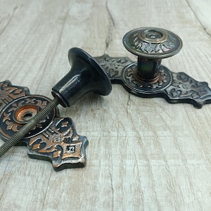 May include: A pair of ornate black and copper door knobs with intricate designs. The knobs have a decorative, vintage style.