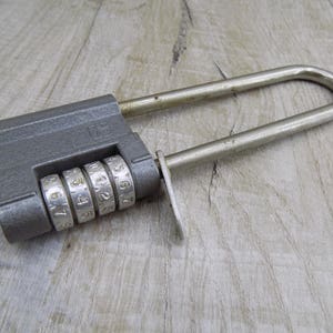 May include: A silver combination padlock with four numbered dials. The padlock is closed and has a gray metal body.
