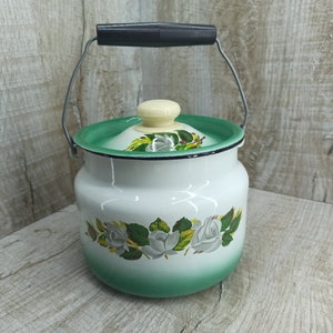 Puede incluir: Olla de esmalte blanco con tapa verde y diseño floral con rosas blancas y hojas verdes. La olla tiene un asa de metal.