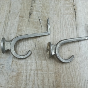 May include: Two silver metal hooks with a curved design. The hooks are mounted on a wooden surface.