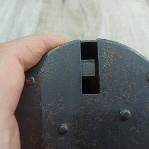 May include: A black metal object with a rectangular opening and several small rivets. The object has a worn, aged appearance.