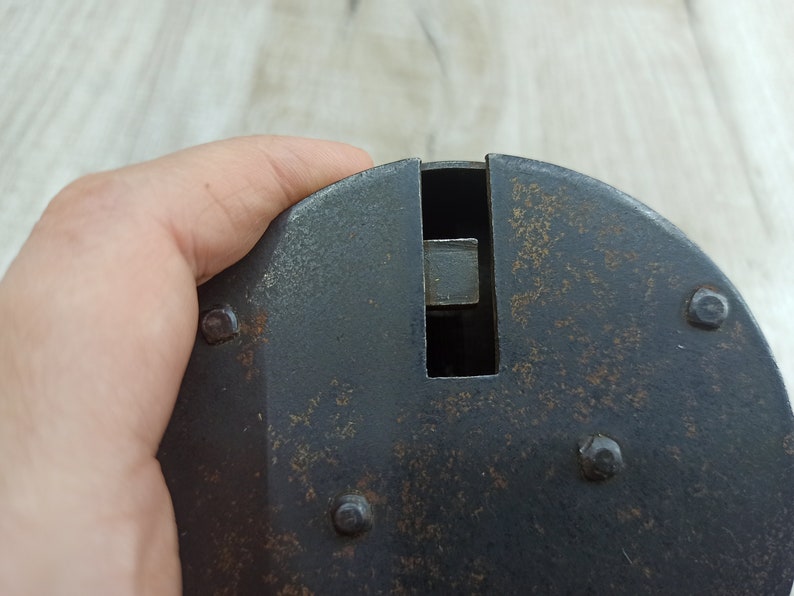 May include: A black metal object with a rectangular opening and several small rivets. The object has a worn, aged appearance.