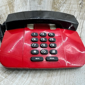 May include: A red rotary phone with a black handset and a keypad with numbers 1 through 9, a star, a zero, and a pound sign. The phone has buttons labeled "Mute" and "Redial".