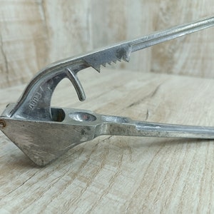 May include: A silver metal garlic press with a lever and a textured surface. The press has the number "2003" stamped on the side.