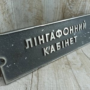 Op de afbeelding: Een zwart metalen bord met witte letters met de tekst "Lingafonni Kabinet".