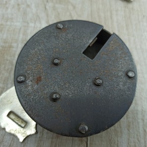 May include: A close-up of a rusty metal lock with a keyhole and several rivets. The lock is circular and has a dark gray finish.