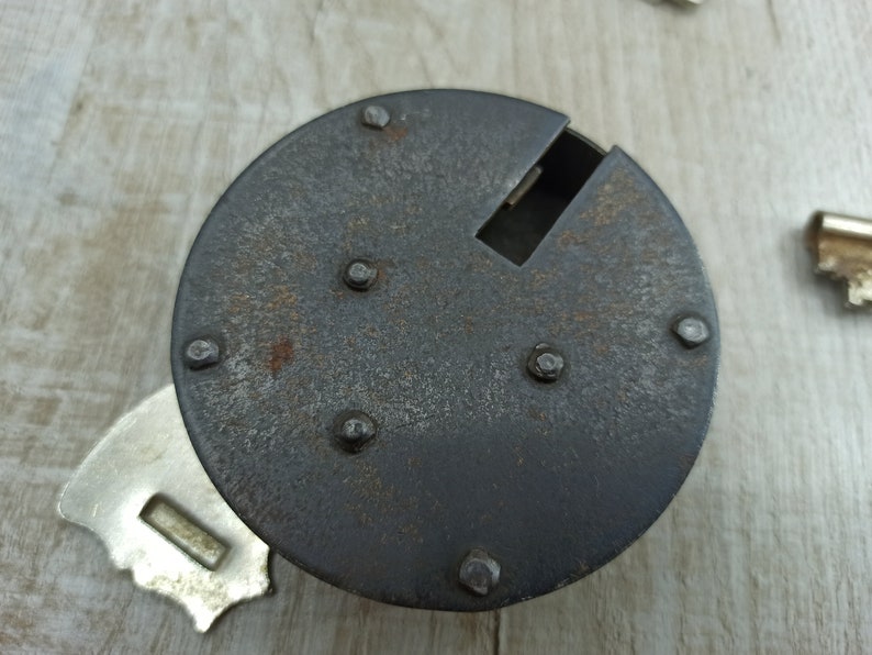 May include: A close-up of a rusty metal lock with a keyhole and several rivets. The lock is circular and has a dark gray finish.