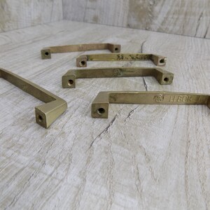 Op de afbeelding: Vijf messing kastgrepen met een rechthoekige vorm en afgeronde randen. De grepen hebben een geborstelde afwerking en zijn gemarkeerd met de tekst "L 80K 7".