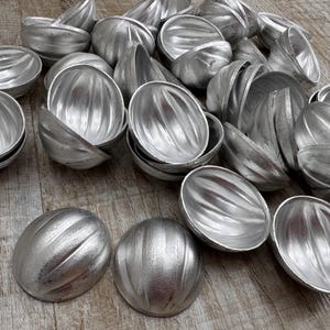 May include: A collection of silver-colored metal molds shaped like half a sphere with a ribbed texture. The molds are arranged in a pile on a wooden surface.