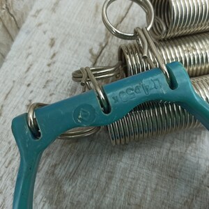 May include: A teal blue exercise equipment with a silver spring coil. The equipment has a handle on each side and the text "L.A. Body" is printed on the teal blue handle.