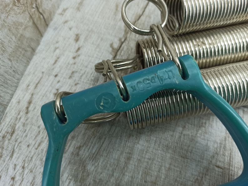 May include: A teal blue exercise equipment with a silver spring coil. The equipment has a handle on each side and the text "L.A. Body" is printed on the teal blue handle.