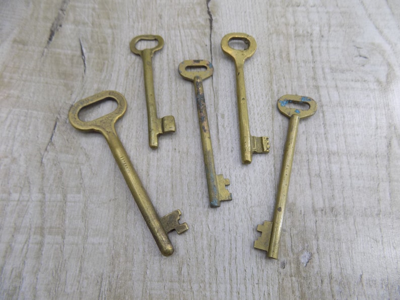 May include: Six antique brass keys of varying sizes and shapes, arranged on a light brown wooden surface.
