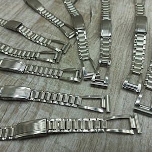 Puede incluir: Una colección de correas de reloj plateadas con diferentes estilos y diseños. Las correas son de metal y tienen un acabado pulido.