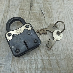 May include: A black padlock with a silver keyhole and two matching keys. The padlock has a silver plate with the letters "SNB" on it.