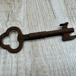 Może przedstawiać: Duży, zardzewiały metalowy klucz z główką w kształcie koniczyny i ząbkowanym brzegiem. Klucz jest oznaczony "1453".