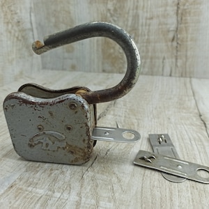 May include: A vintage padlock with a silver finish and a rusty patina. The padlock has a keyhole and a metal loop for attaching to a chain or other object. The padlock is accompanied by two keys.