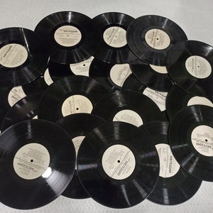 Pode incluir: Uma coleção de discos de vinil pretos empilhados uns sobre os outros. Os discos têm etiquetas brancas com texto.