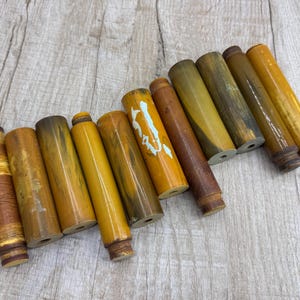 May include: A collection of ten brown and yellow wooden dowels with a variety of patterns and textures.