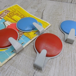 May include: Four adhesive hooks with a round base and a silver hook. Two hooks are red and two are blue.