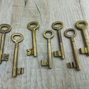 May include: A collection of eight antique brass keys with intricate designs. The keys are arranged on a light wood surface.