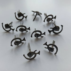 Könnte beinhalten: Zehn schwarze Metallnadeln mit einem stilisierten Design aus einer Mondsichel und einem Stern. Die Nadeln sind in einem Kreis auf einer weißen Oberfläche angeordnet.