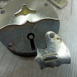 May include: A vintage silver padlock with a keyhole and a decorative design on the top. The padlock has a rusty brown finish and a silver metal latch.