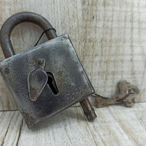 May include: A rusty metal padlock with a keyhole and a matching key. The padlock is closed and has a worn, aged appearance.