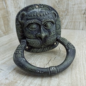 以下が含まれることがあります： 複雑なディテールが施されたライオンの頭の形をした黒い金属製のドアノッカー。ノッカーにはリングハンドルが付いており、伝統的なスタイルでデザインされています。