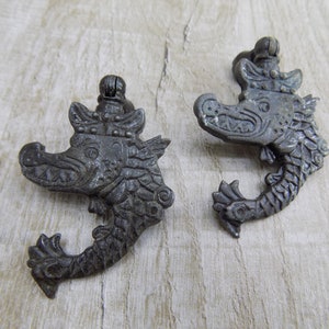 May include: Two antique silver-toned pendants shaped like a dragon with a crown on its head. The pendants are detailed with scales and have a loop at the top for hanging.