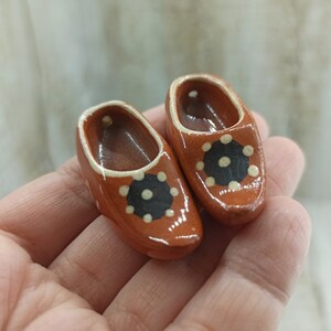 Puede incluir: Dos pequeños zuecos de cerámica marrón con diseños de lunares blancos y negros.