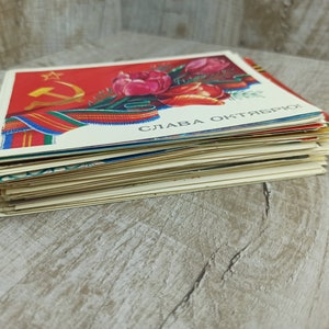 May include: A stack of vintage postcards featuring a red background with a gold star, hammer and sickle, and a bouquet of red tulips. The postcards have text in a foreign language.