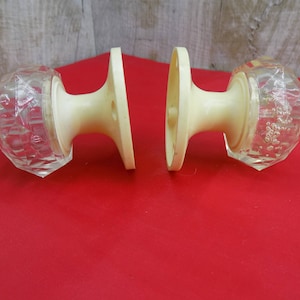May include: Two white door knobs with clear glass accents. The glass is textured and has a faceted design.