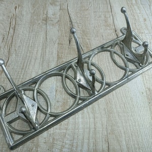Puede incluir: Perchero de metal plateado con un diseño decorativo de círculos entrelazados. El perchero tiene cinco ganchos.