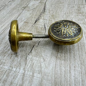 May include: A brass door knob with a decorative floral design. The knob is attached to a metal rod.