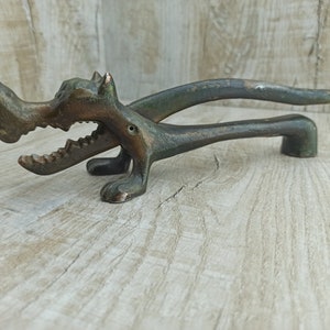 Può includere: Un schiaccianoci color bronzo a forma di cane con la bocca aperta e denti affilati. La testa del cane è inclinata di lato e la coda è arrotolata.