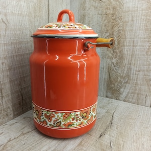 Könnte beinhalten: Orangefarbene Email-Milchkanne mit einem floralen Muster am Boden. Die Kanne hat einen Holzgriff und einen Deckel mit einem floralen Muster.