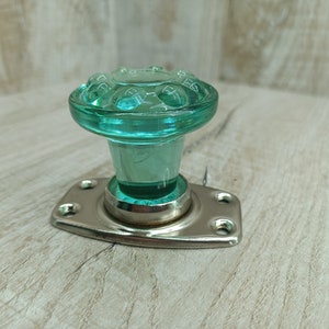 Può includere: Una manopola per porta vintage in vetro verde con un design decorativo e una base in metallo argentato.