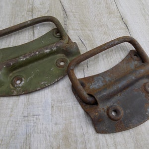 May include: Two vintage metal handles with a rusty finish. One handle is painted green and the other is a dark gray. Both handles have a curved shape and a metal loop for lifting.