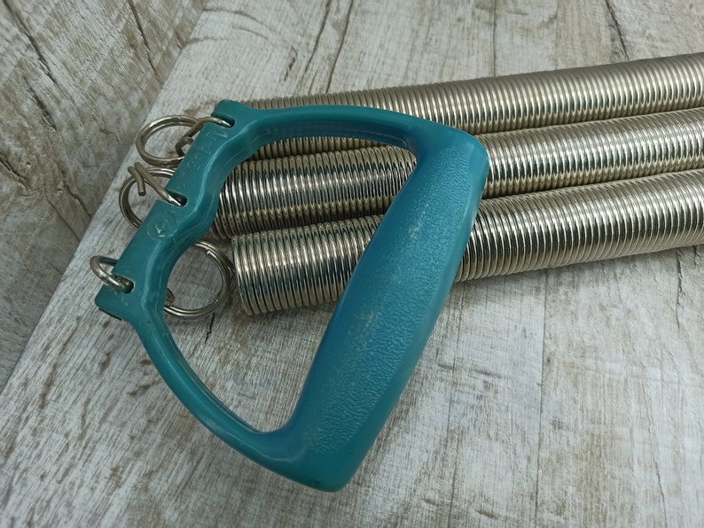 May include: A teal exercise expander with multiple silver springs. The expander has a handle with a loop on each end.
