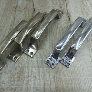 May include: Set of five silver-toned metal door handles. Three handles have a more ornate design and two have a simpler design.