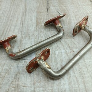 Könnte beinhalten: Zwei vintage Metallgriffe mit roter Lackierung. Die Griffe sind U-förmig gebogen und haben eine flache rechteckige Basis.