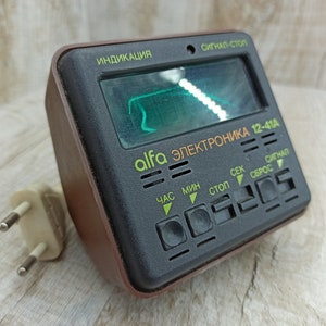 May include: A black and brown electronic device with a green screen and the text "alfa электроника 12-41A". The device has buttons labelled "час", "мин", "стоп", "сек", "сброс", and "сигнал".