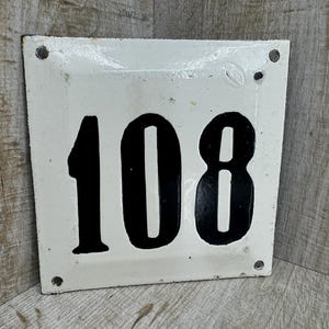 May include: White enamel house number sign with black numbers reading "108".