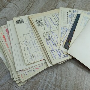 May include: A collection of vintage postcards, featuring handwritten messages, stamps, and postmarks. The postcards are in various sizes and orientations, with a mix of colors and designs. Some cards have text in a foreign language.