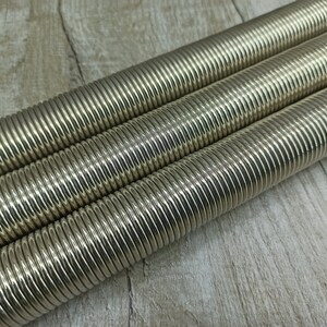 May include: Three silver-coloured metal springs, coiled and stacked on top of each other, on a light brown wooden surface.