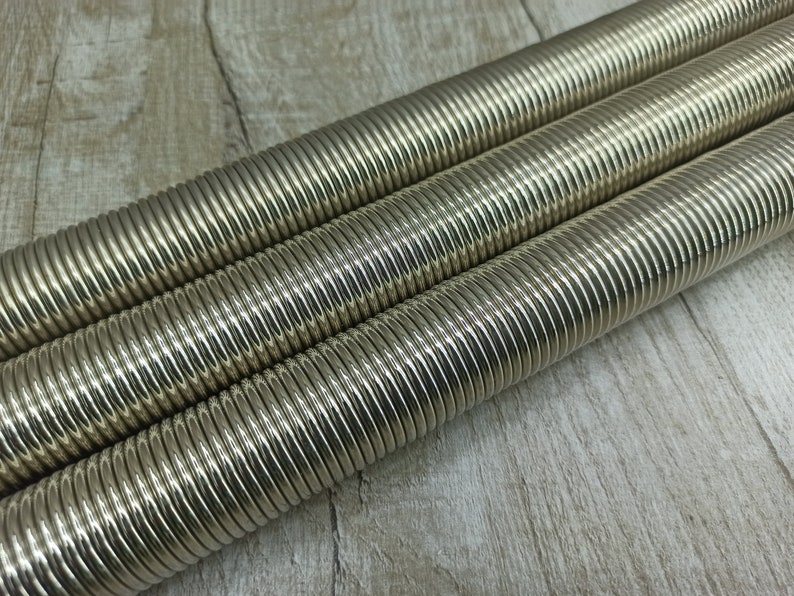 May include: Three silver-coloured metal springs, coiled and stacked on top of each other, on a light brown wooden surface.
