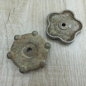 May include: Two antique metal knobs with a circular shape and a hole in the center. The knobs have a worn, aged appearance and are made of a dark gray metal.