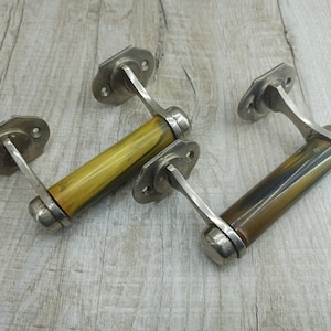 Può includere: Due maniglie per porte antiche con finitura marmorea gialla e marrone. Le maniglie sono in metallo e hanno un design decorativo.